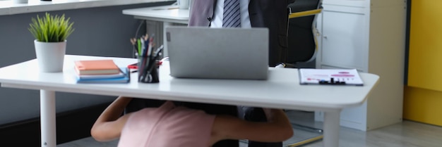 Tevreden mannelijke baas achter bureau en vrouw molesteert onder tafel