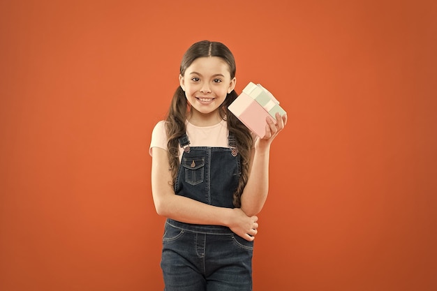 Tevreden met winkelen klein kind met geschenkdoos op oranje achtergrond klein meisje na het winkelen voor cadeau schattige jongen genieten van winkelen winkelverslaafde met cadeau verpakt in doos