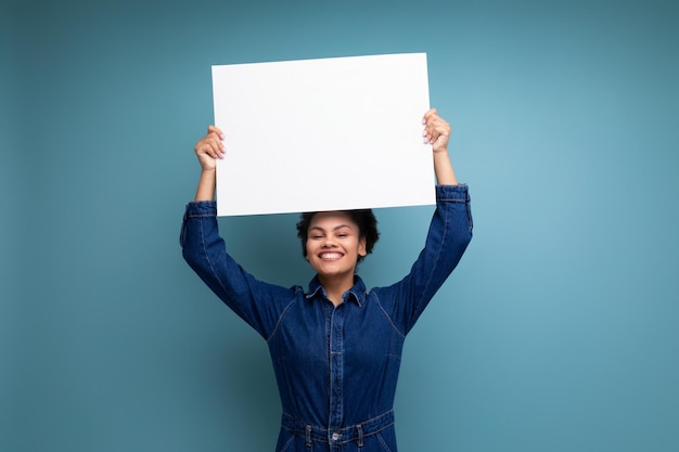 Tevreden positieve jonge Spaanse brunette vrouw met pluizig krullend haar in blauw denim pak met een