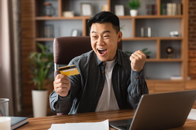 Tevreden verrast opgewonden volwassen japanse zakenman met open mond houd creditcard win gebaar maken