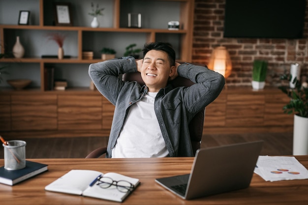 Tevreden volwassen Japanse man rustend in stoel aan tafel in kantoorinterieur