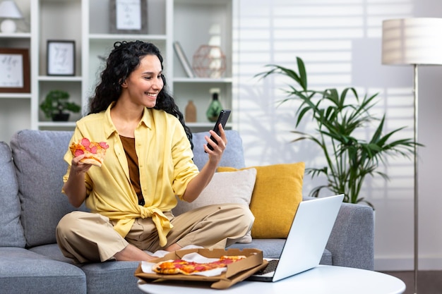 Tevreden vrouw thuis ontspannen zittend op de bank in de woonkamer en het eten van pizza Spaanse vrouw