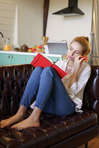 Foto tevreden vrouwelijke persoon die op een leren bank zit en een broodje eet