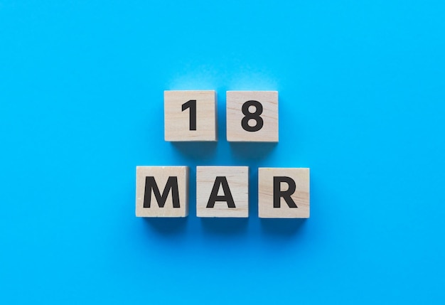 Text 18 MAR MARCH on wooden cubes on BLUE background Date Square wood blocks Top view flat la