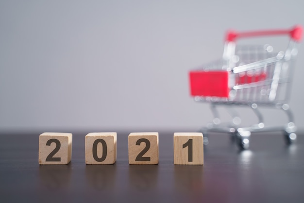 Text 2021 on wooden cube with shopping cart isolated on gray. New year countdown concept.