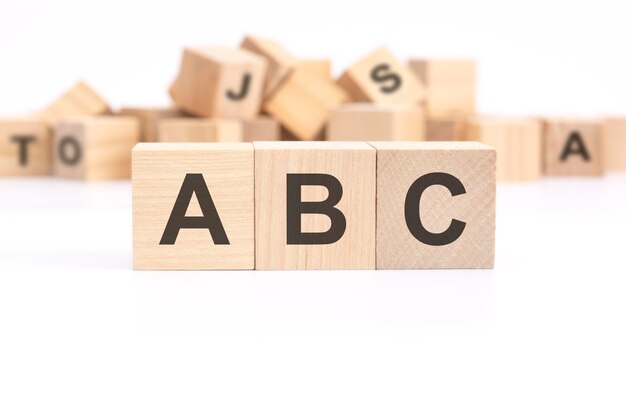 Text ABC Always Be Closing is written on three wooden cubes standing on a white table in the background a mountain of wooden cubes with letters