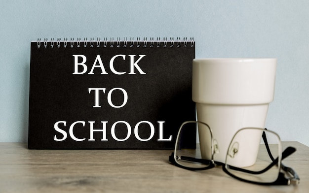 Text BACK TO SCHOOL . mug, glasses, black notebook for information on the wooden table