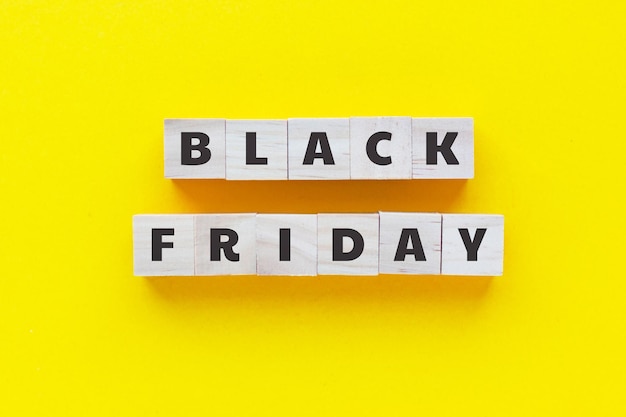 Text BLACK FRIDAY on wooden cubes on yellow background. Big sale. Square wood blocks. Top view, flat lay.