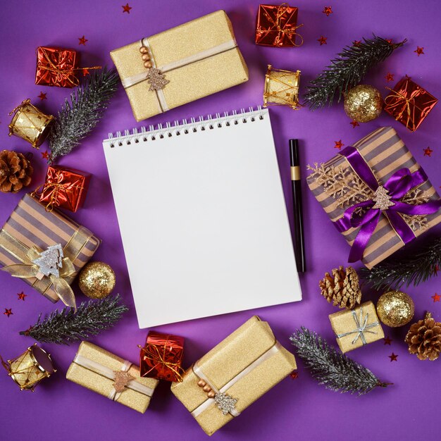 Text book with empty pages and golden marker among gift boxes and presents on violet background