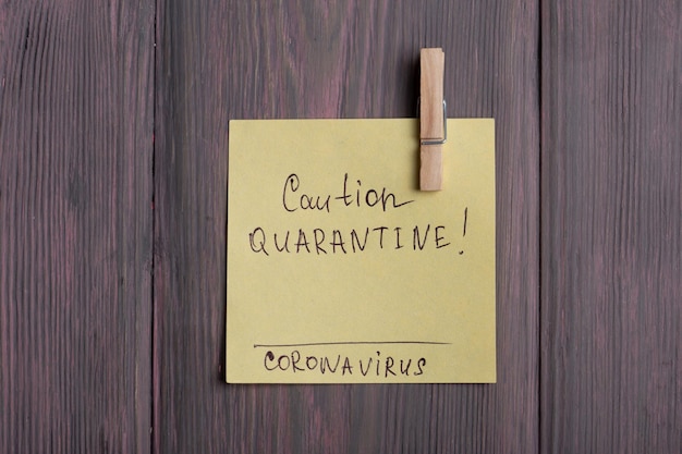 Text Caution Quarantine Coronavirus on sticky note that hangs with a clothespin on wooden background