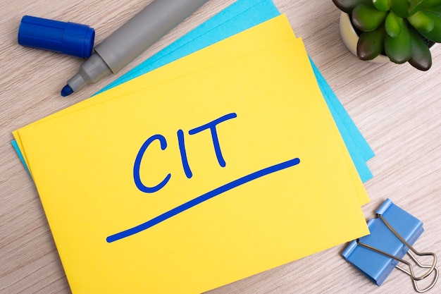 Text CIT on yellow paper on light wooden background with stationery