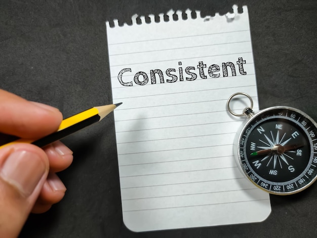 Text Consistent writing on notepaper with hand holding pencil and compass on black background