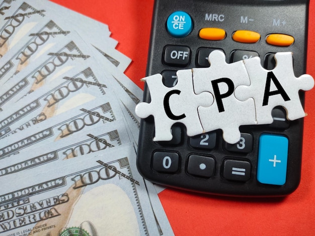 Text CPA Cost Per Action writing on jigsaw puzzle with fake money and calculator on red background