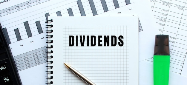 Text DIVIDENDS on the page of a notepad lying on financial charts