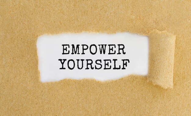 Foto testo empower yourself che appare dietro carta marrone strappata