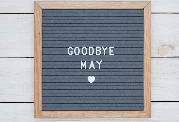 Photo text in english goodbye may and a heart sign on a gray felt board in a wooden frame.
