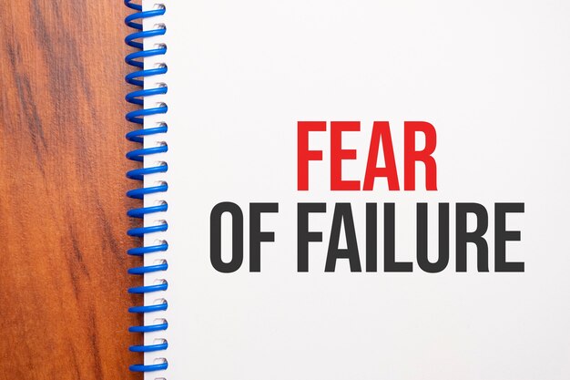 Текст «Страх неудачи», написанный в блокноте, офисный деревянный стол сверху, концептуальное изображение для заголовка блога или изображения заголовка. Выдержанный винтажный цвет.