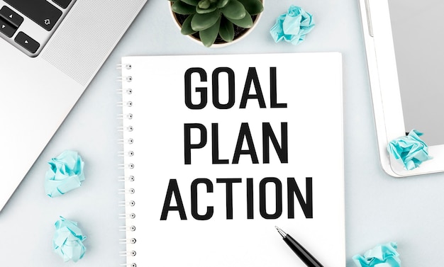 Text GOAL PLAN ACTION on note. Laptop, pieces of paper, pen and plant on office desk. Flat lay, top view. Planning concept.