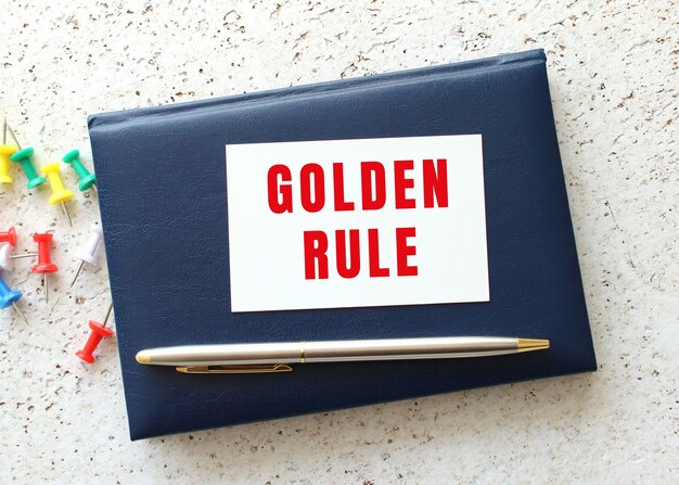 Photo text golden rule on a business card lying on a blue notebook next to the pen. business concept.