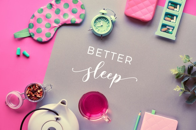 Text "Good Better sleep". Pills, capsules and calming tea. Flat lay, two tone coral and craft paper wall Pink sleeping mask with polka dots, alarm, earphones and earplugs