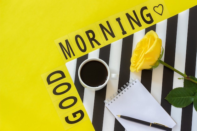 Text good morning, cup of coffee, donut, rose, notepad concept stylish workplace