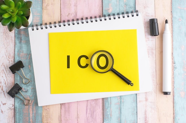 text ICO under a magnifying glass on a yellow background top view the text is written in black marker