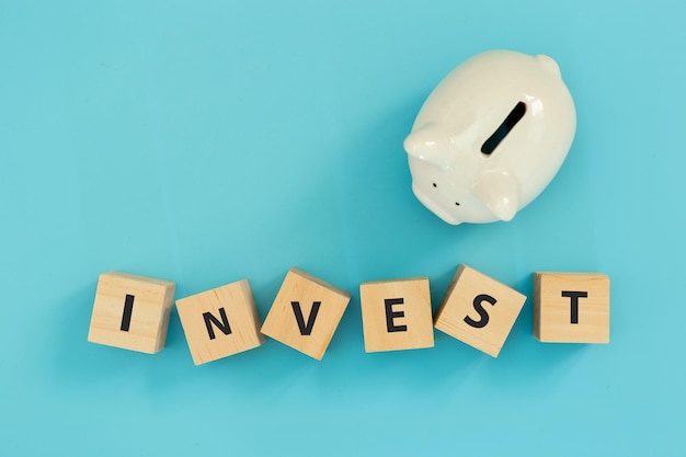 Foto testo investire su blocco cubo di legno con salvadanaio bianco su sfondo blu concetto di investimento investire in risparmi per il futuro
