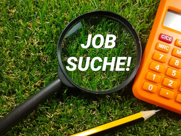 Text job suche on magnifying glass with pencil and calculator\
on grass background