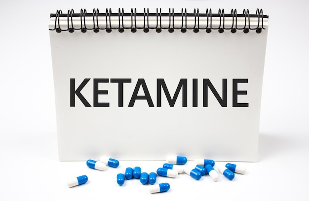 Text KETAMINE on a notepad next to the capsules