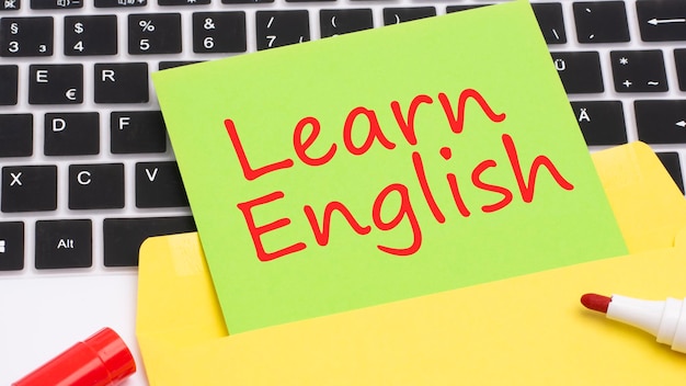 텍스트 LEARN ENGLISH는 프레임의 녹색 카드에 빨간색 마커로 작성되어 비즈니스 및 금융의 노란색 메모장 개념에 있는 노트북 키보드입니다.