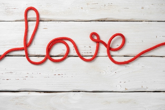 Photo text love from red rope on white wooden background