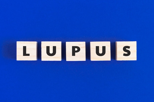 青い背景の木製の立方体にテキストLUPUS。自己免疫疾患、医学の概念。上面図、フラットレイ。