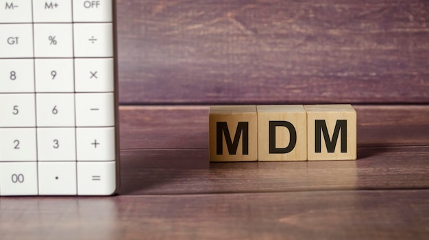 Text MDM as MOBILE DEVICE MANAGEMENT on wooden blocks and calculator