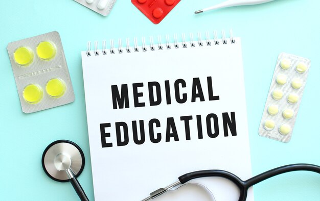 The text MEDICAL EDUCATION is written in a notebook that lies next to the stethoscope, medicine on a blue background