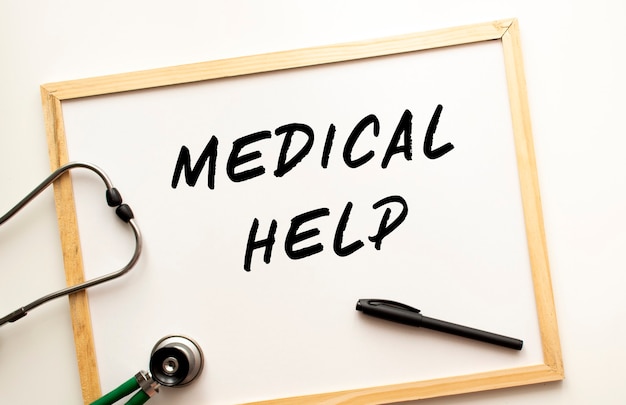 MEDICAL HELP 텍스트는 마커가있는 흰색 사무실 보드에 작성됩니다. 근처에는 청진기가 있습니다. 의료 개념.