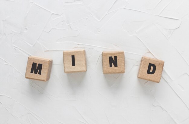 Text MIND made of wood cubes on white textured putty background. Square wood blocks. Top view, flat lay.