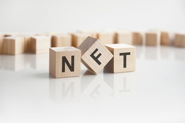 Text NFT on wooden blocks with letters on a white background reflection of the caption on the mirrored surface of the table