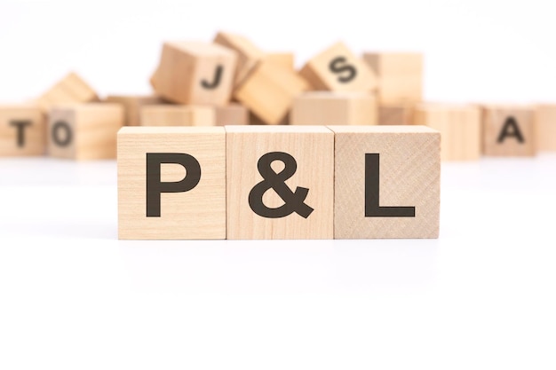 Text P and L profit and loss is written on three wooden cubes standing on a white table in the background a mountain of wooden cubes with letters