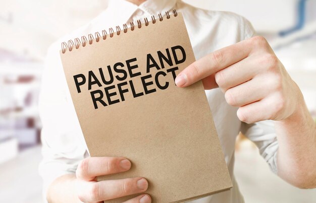 Text PAUSE AND REFLECT on brown paper notepad in businessman hands in office Business concept