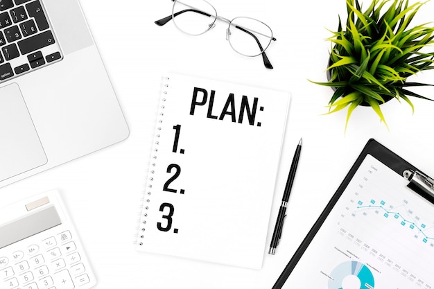 Text PLAN on card. Laptop, calculator, clipboard for chart, glasses, pen and plant on office desk. Flat lay, top view. Planning concept.