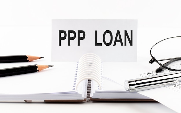 Text PPP LOAN on paper card,pen, pencils, glasses, and financial documentation on the table