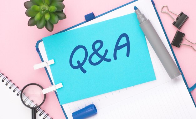 text Q and A on blue paper composition with stationery on color pink background top view