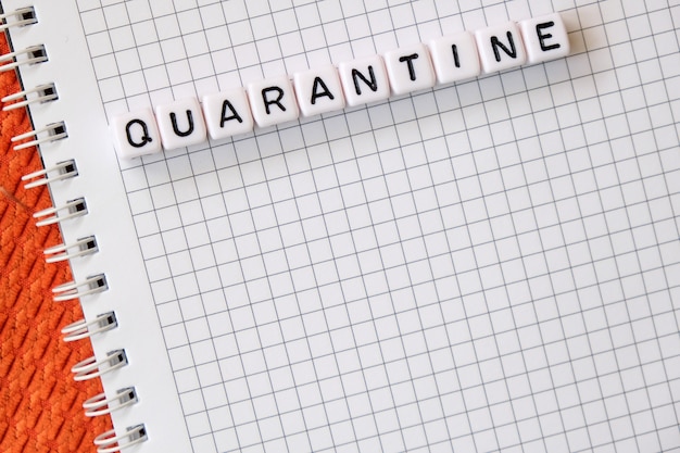 Text Quarantine , word made of cubic letters on a white paper note pad background