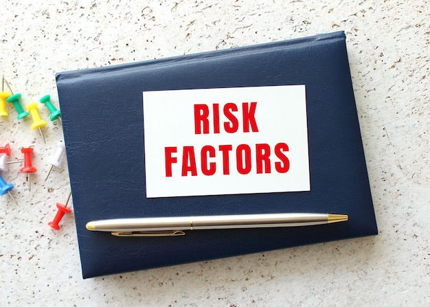 사진 펜 옆에 있는 파란색 공책에 누워 있는 명함의 risk factor 텍스트