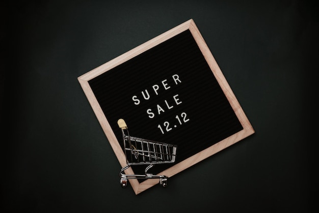 Photo the text of the sale 12.12 on a letter board with a mini grocery cart. design to promote the winter sale at the end of the year. top view. solid green background