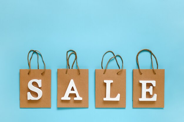 Photo text sale from white volume letters and blank shopping bags on blue background.