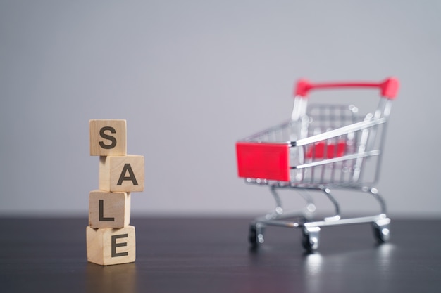 Text "SALE" on wooden cube with shopping cart isolated on gray.