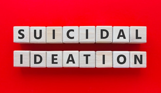 Text Suicidal Ideation on wooden cubes. Suicidal thoughts. Prevention. Mental health, mind problem, disorder and depression. Flat lay, top view on red background.