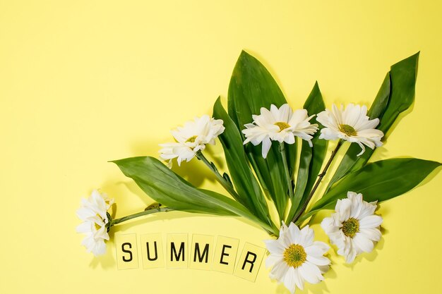 Text SUMMER from letters and field chamomiles flowers on yellow background