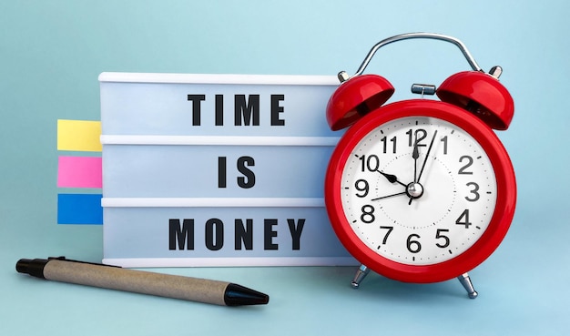Photo text time is money written on the lightbox with alarm clock and colorfull stickers on blue background